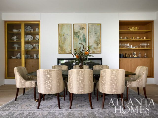 Dining room with a dark wood table surrounded by upholstered chairs with a light-colored animal print. Features built-in wood cabinetry with glass doors displaying dishes and a bar area with glassware.