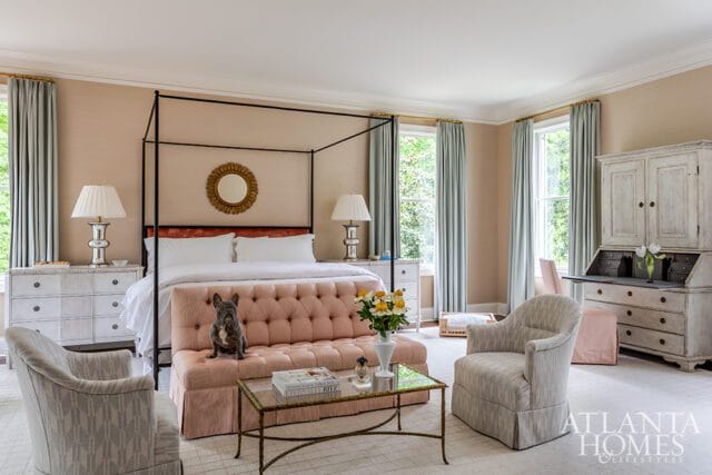 Bedroom with a four-poster bed, tufted pink sofa, French bulldog, antique secretary desk, and light blue curtains.