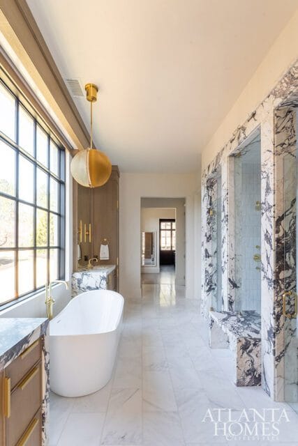 Spacious bathroom with a freestanding white tub, marble-clad shower stalls with glass doors, and a vanity with marble countertop and wood cabinetry.