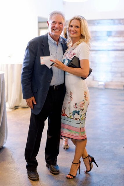 Man in a navy blazer and woman in a floral dress smiling at an event.