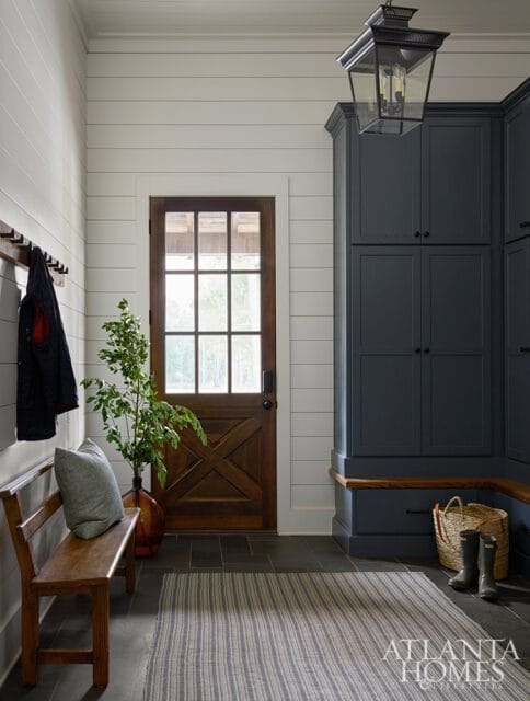 Mudroom with shiplap walls, a wooden bench, dark blue built-in cabinets, and a rustic wooden door with glass panes.