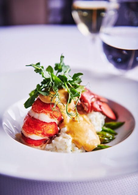 Butter poached lobster tail served over risotto with asparagus and topped with a creamy sauce and microgreens.