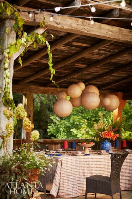 Outdoor dining table set under a wooden pergola with string lights and paper lanterns.