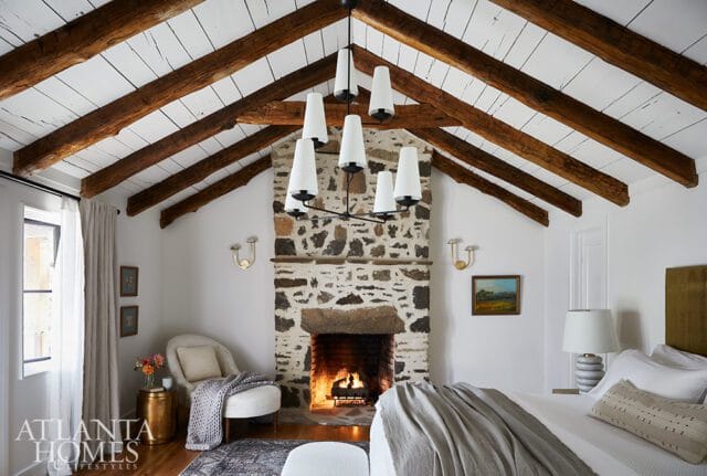 Bedroom with stone fireplace, vaulted wood beam ceiling, and white walls.
