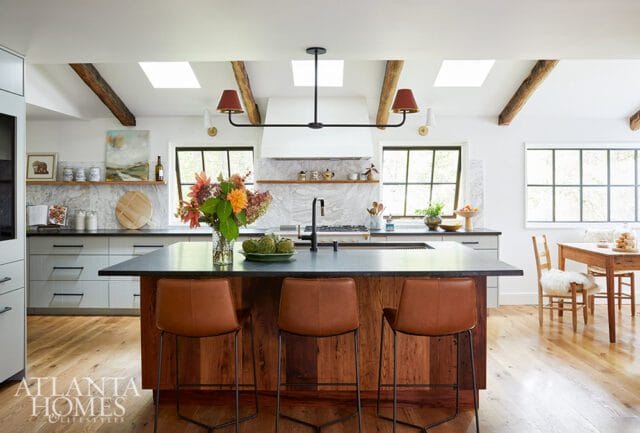Kitchen island with leather stools, wood paneling, and dark countertop. Skylights and exposed beams