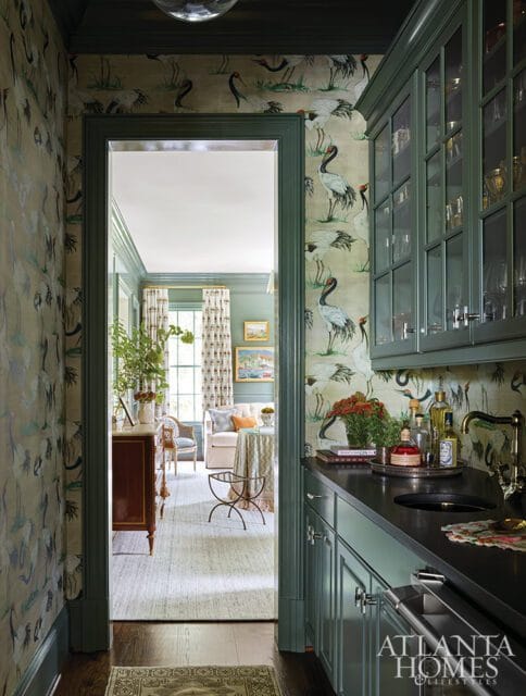 Hallway with crane-patterned wallpaper and a dark countertop wet bar with glass-front cabinets. A doorway opens to a living area with a sofa and table.