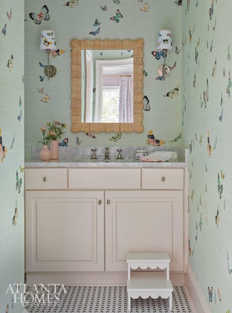 Powder room with light green butterfly wallpaper, a marble vanity with a rattan mirror, and a cream-colored cabinet.