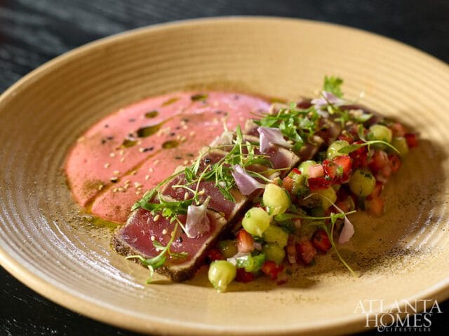 Seared tuna slices served with a pink puree, diced strawberries, and cucumber on a ribbed tan plate, with Atlanta Homes & Lifestyles logo in the corner.