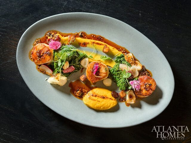 Seared scallops with puree, greens, radishes, and edible flowers on a light blue plate, with Atlanta Homes & Lifestyles logo in the corner.