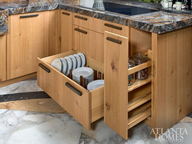 Light wood kitchen cabinets with dark hardware, featuring an open drawer with stacked plates and a pull-out pantry with glass jars of candy and snacks.