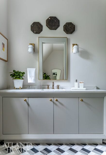 Gray bathroom vanity with marble countertop, brass hardware, and a gold-framed mirror. Octagonal wall art hangs above the mirror.