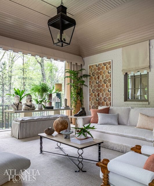 Covered porch with white brick walls, a large black lantern, and a sofa with light-colored upholstery and fringe trim.