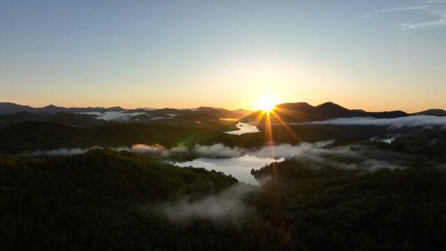 Sunrise over misty mountains and lakes, with sunbeams radiating from the horizon and illuminating the landscape.