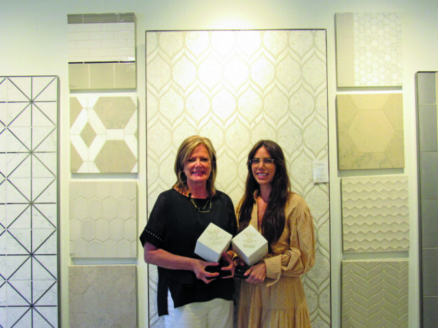 Two women holding awards in front of a wall of decorative tiles.