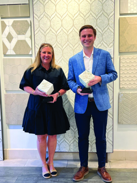 Woman in black dress and man in blue blazer holding awards in front of tile samples