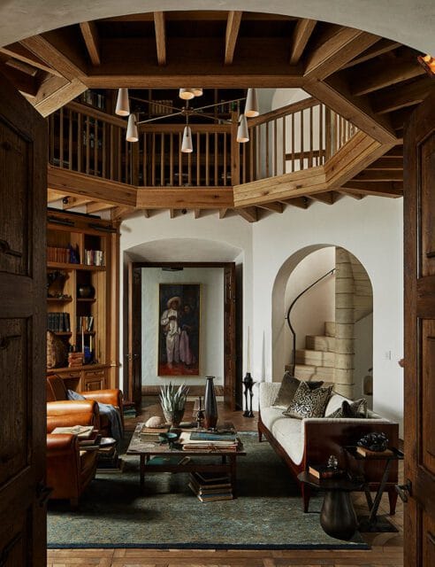 Living room with wood beams, built-in bookshelves, leather chairs, and a spiral staircase.