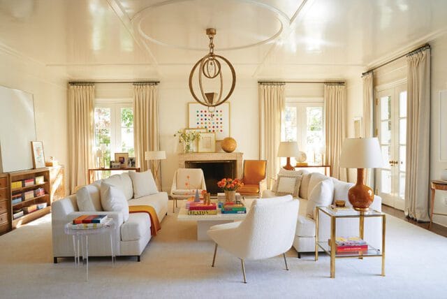Living room with white sofas, fireplace, colorful artwork, and ornate chandelier.