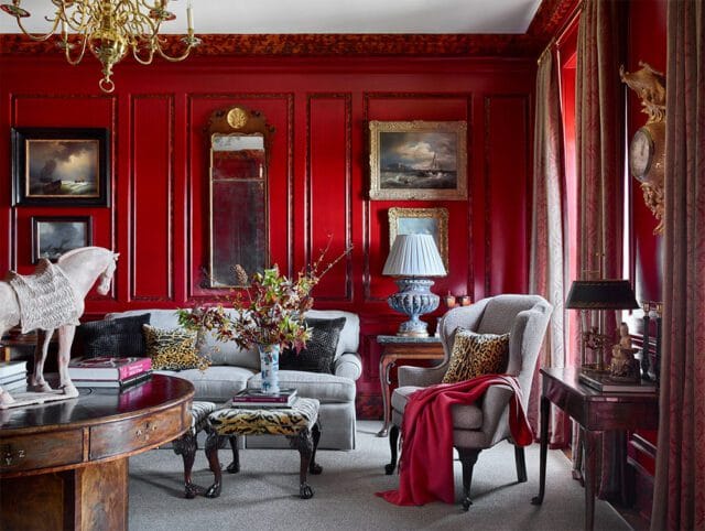 Red paneled living room with gray sofa, armchair, and ornate chandelier.