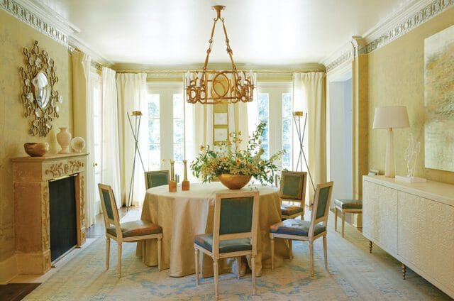 Dining room with a round table, floral centerpiece, ornate chandelier, and fireplace.