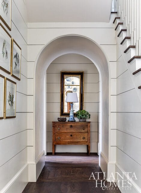 Hallway with shiplap walls, arched doorway, antique dresser, mirror, and staircase