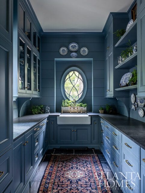 Blue kitchen with farmhouse sink, oval window, and patterned rug