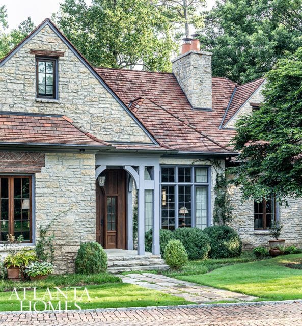 Stone house with red tile roof, arched entryway, and large windows.