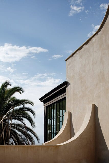 Modern building exterior with curved stucco walls, dark framed windows, and palm tree.