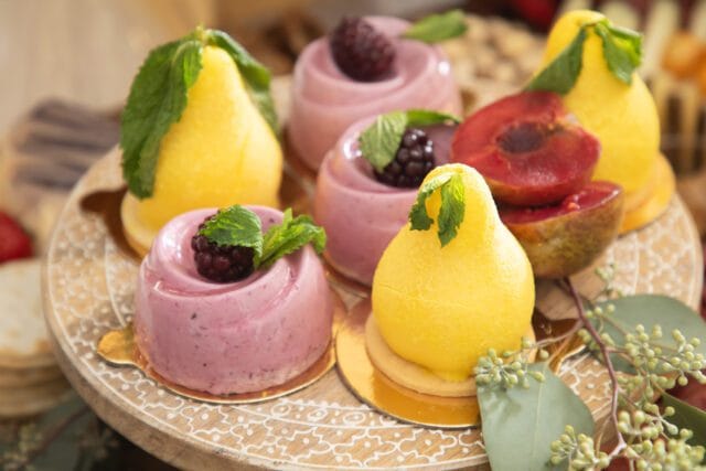 Assortment of small berry mousse cakes and pear-shaped pastries garnished with mint leaves and