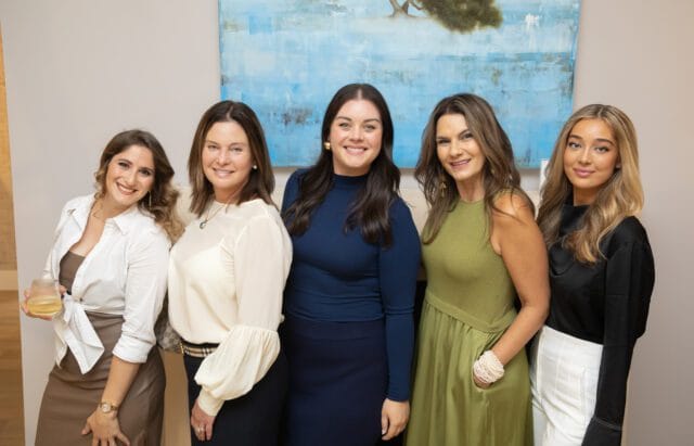 Five women posing for a photo in front of a blue abstract painting.