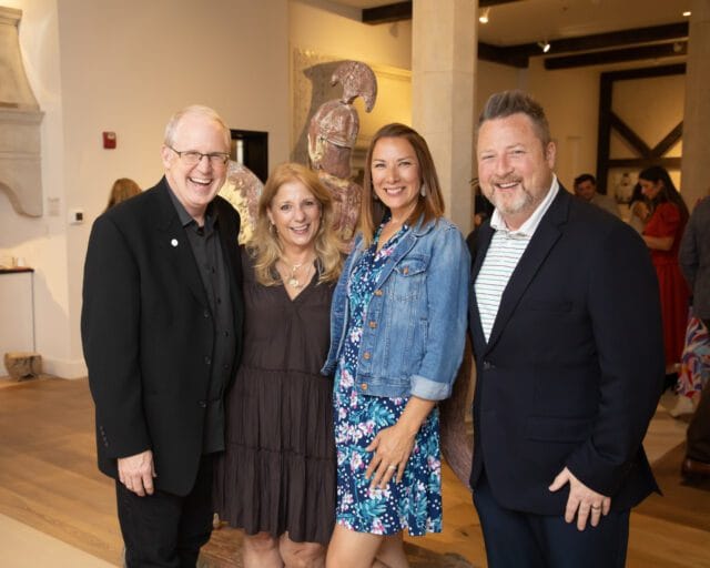 Two couples smiling at the camera in an indoor setting with artwork in the background.