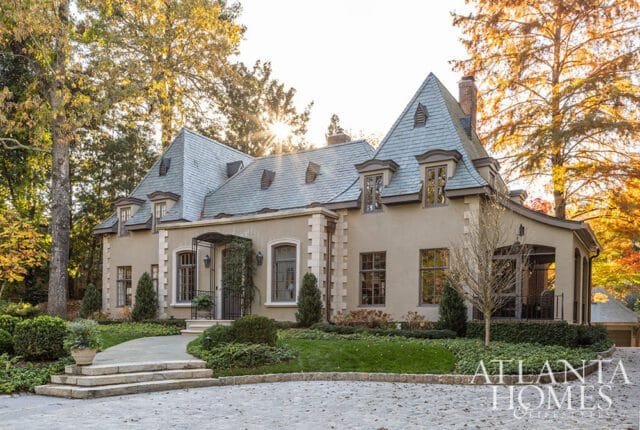 French-style home with tan stucco, gray slate roof, and stone accents.