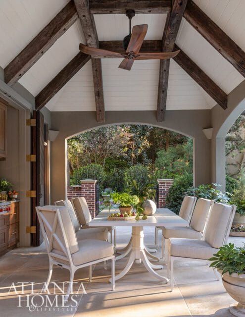 Covered patio with white dining set, ceiling fan, and arched view of garden