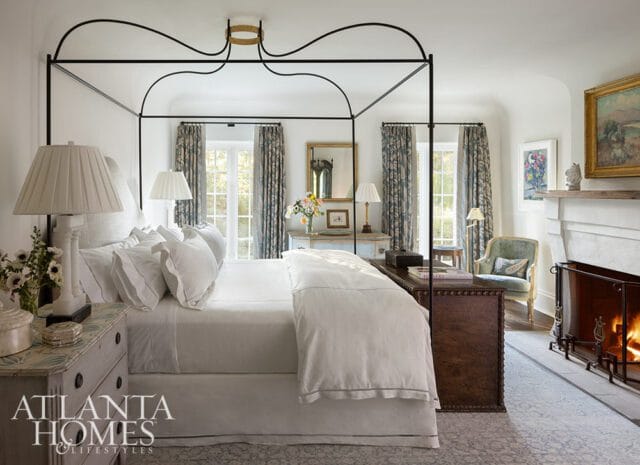 Primary bedroom with a black canopy bed, white bedding, patterned curtains, and a fireplace.