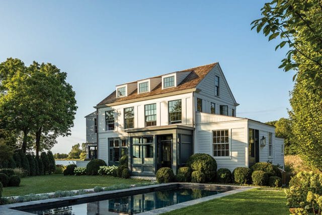 Light gray house with dormer windows and a dark gray sunroom addition next to a pool.