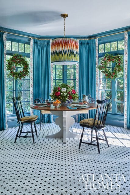 Dining room with teal curtains, round table, floral centerpiece, and black chairs on hex tile floor.