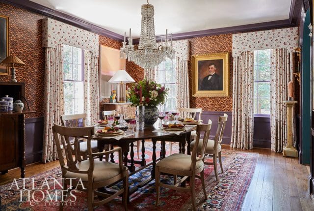 Dining room with patterned wallpaper, floral curtains, and a crystal chandelier.
