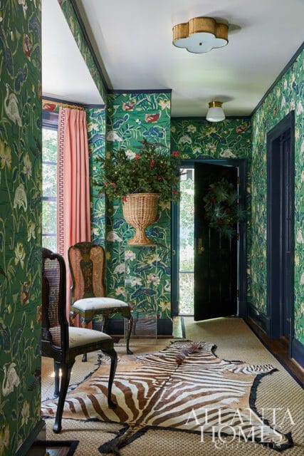 Hallway with green floral wallpaper, zebra rug, cane chairs, and open door with wreath
