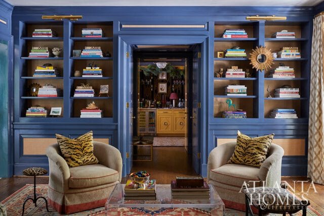 Living room with blue built-in bookshelves, two armchairs with tiger print pillows, and an acrylic