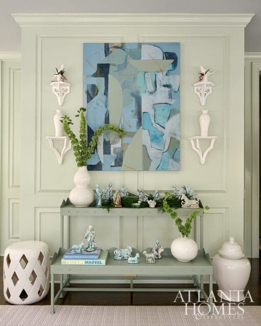 Pale green walls with abstract art, white shelves, vases, and nativity figurines on a console table.