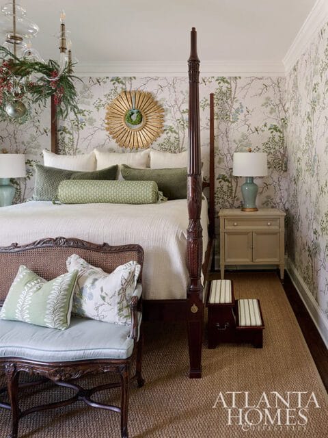 Four-poster bed with botanical wallpaper, green pillows, and a sunburst mirror.