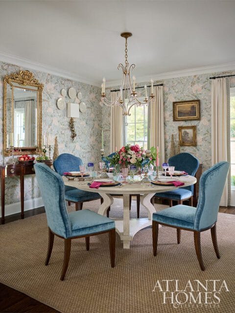 Dining room with blue velvet chairs around a round table set for a meal. Floral centerpiece.