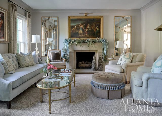 Light blue sofa, glass coffee table, stone fireplace with garland, and tufted ottoman.