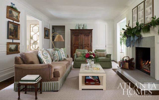 Living room with brown sofa, green armchairs, coffee table, and fireplace decorated for Christmas.