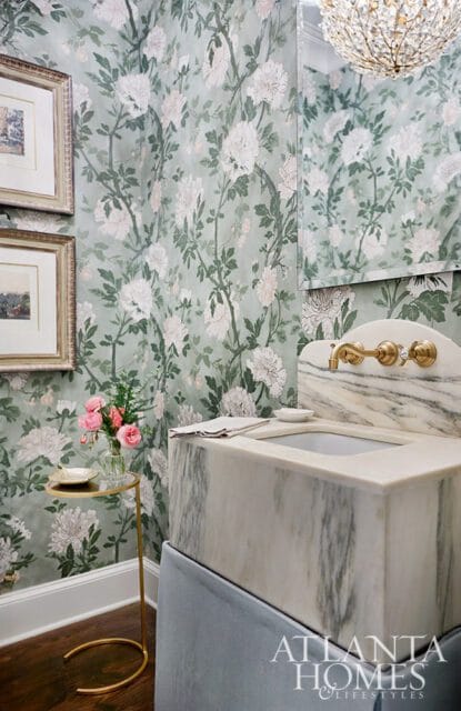 Powder room with floral wallpaper, marble sink, brass faucet, and crystal chandelier.