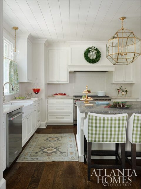 White kitchen with shiplap ceiling, brass lantern, and green gingham bar stools.