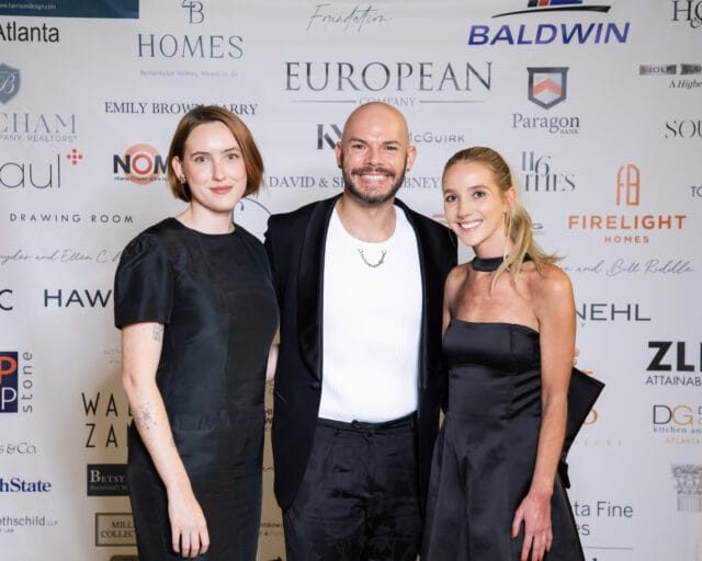 Three people in black formal wear pose in front of a backdrop with sponsor logos.