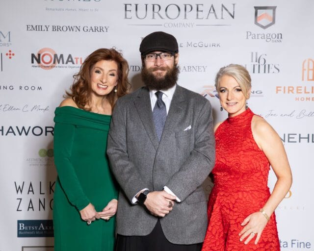Three people posing for a photo in front of a branded backdrop