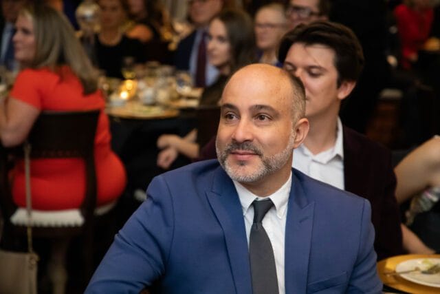 Man in blue suit and dark tie looking to the side at a formal event