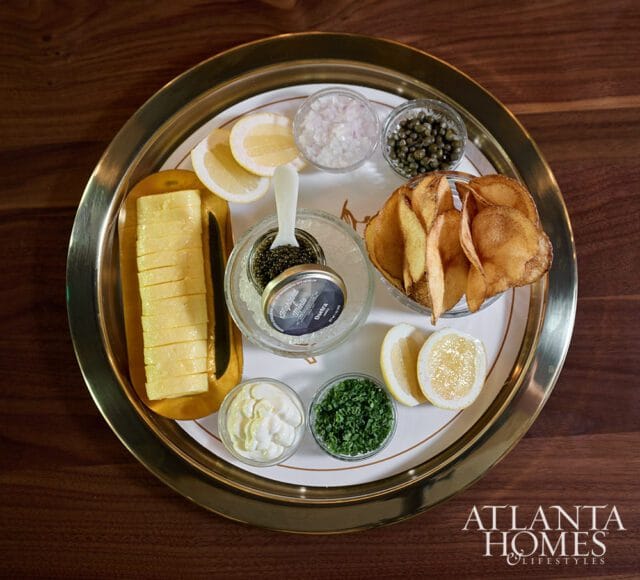 Caviar service with butter, chips, lemons, capers, onions, and chives on a tray.