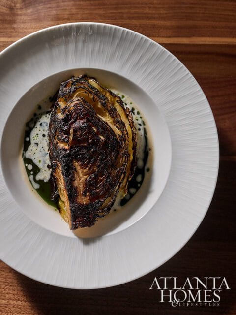 Roasted cabbage wedge in a white bowl with sauce and Atlanta Homes & Lifestyles logo